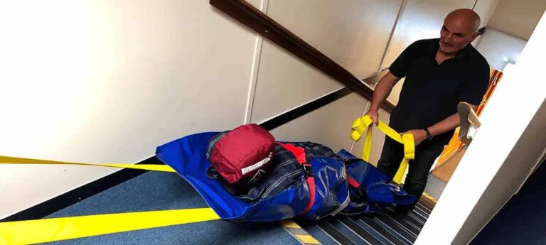 Ski mat evacuation training demonstration - instructor safely evacuating training manikin down stairs using ski evacuation mat with yellow straps - Phoenix STS Nursing Home Fire Safety Training Ireland
