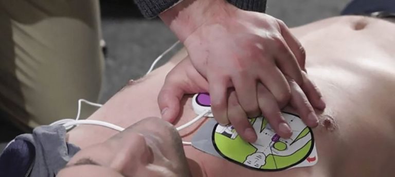 Hands placing AED defibrillator pads on a CPR manikin during a HeartSaver AED Course from Phoenix STS Ireland